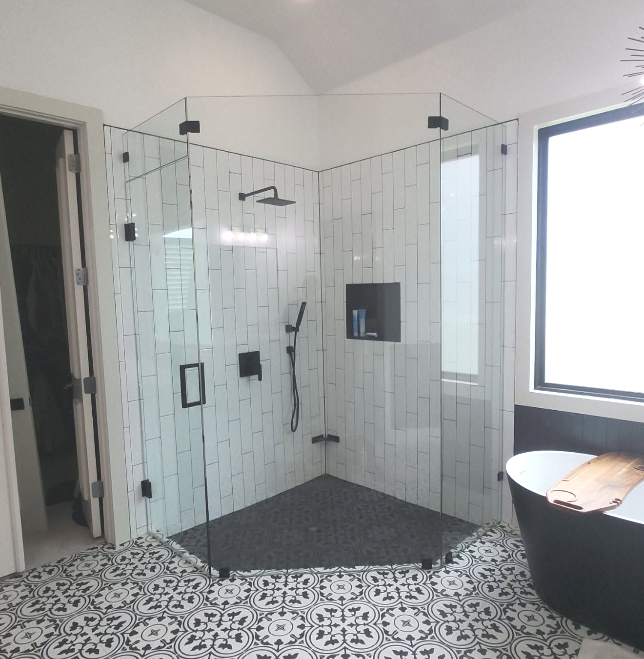 Modern bathroom with glass shower enclosure, black fixtures, white tile, and patterned floor.