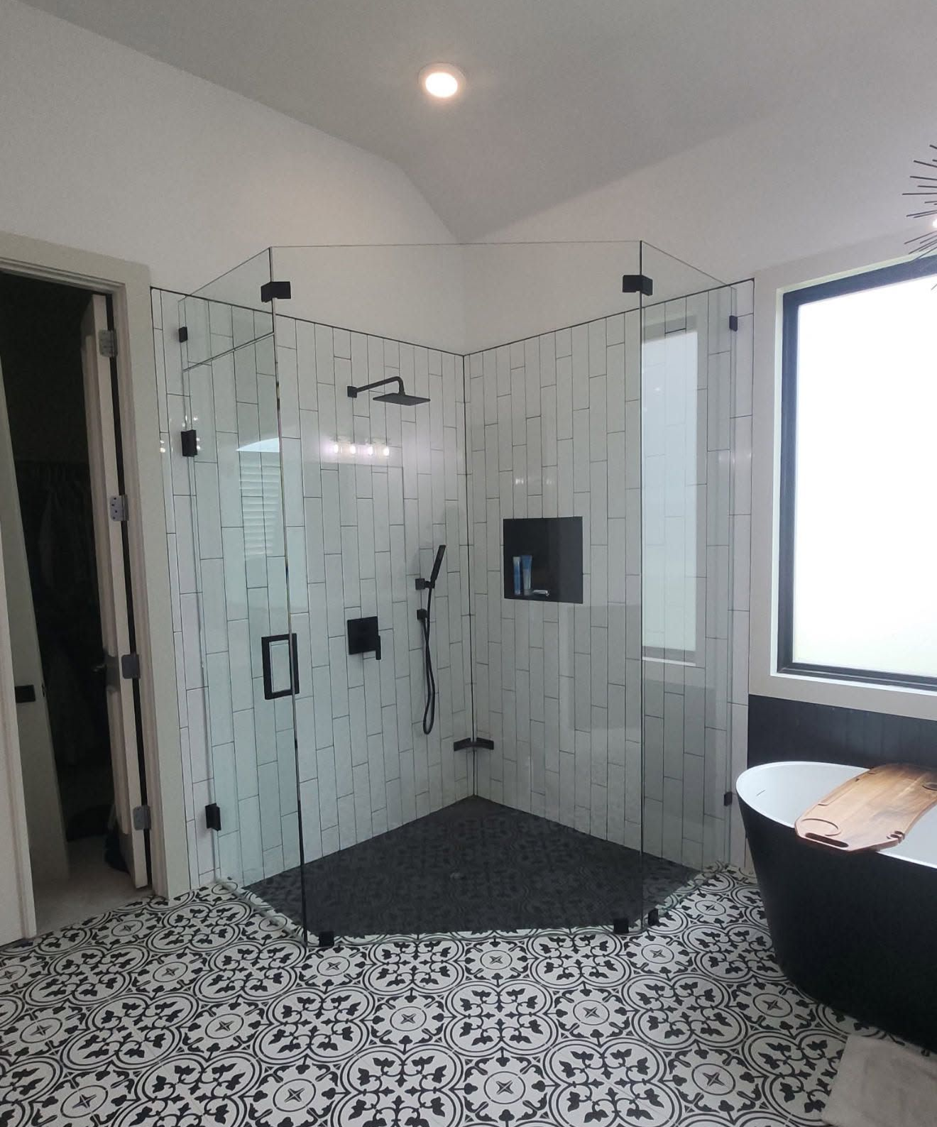 Modern bathroom with glass shower enclosure, white tile walls, black floor, and large window