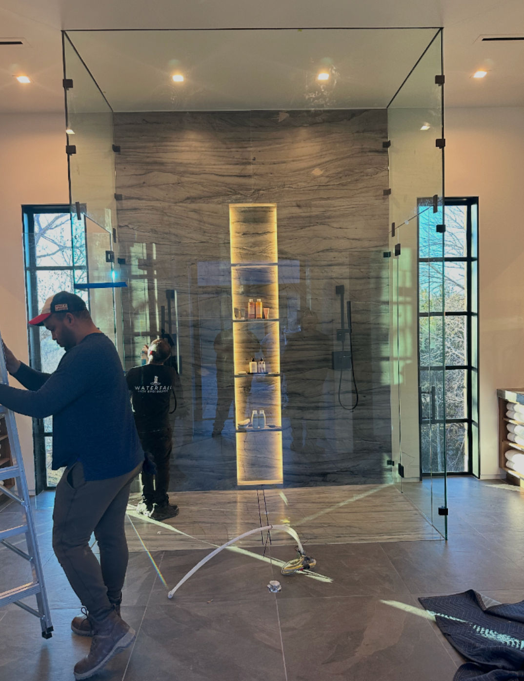 Workers installing a glass display wall in a modern lobby with stone accent wall and lit shelves