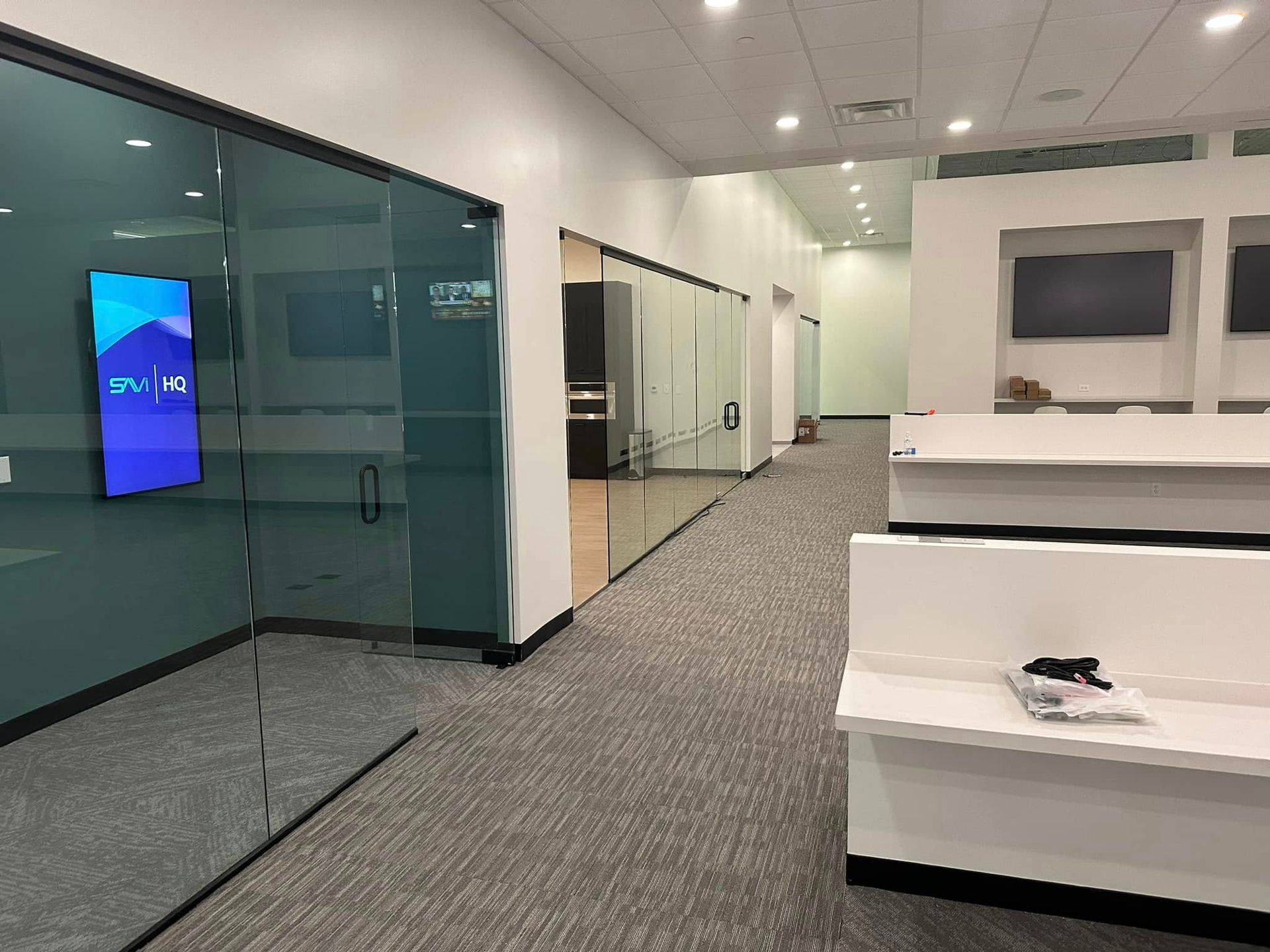 Modern office hallway with glass walls, gray carpet, and white counters in the foreground