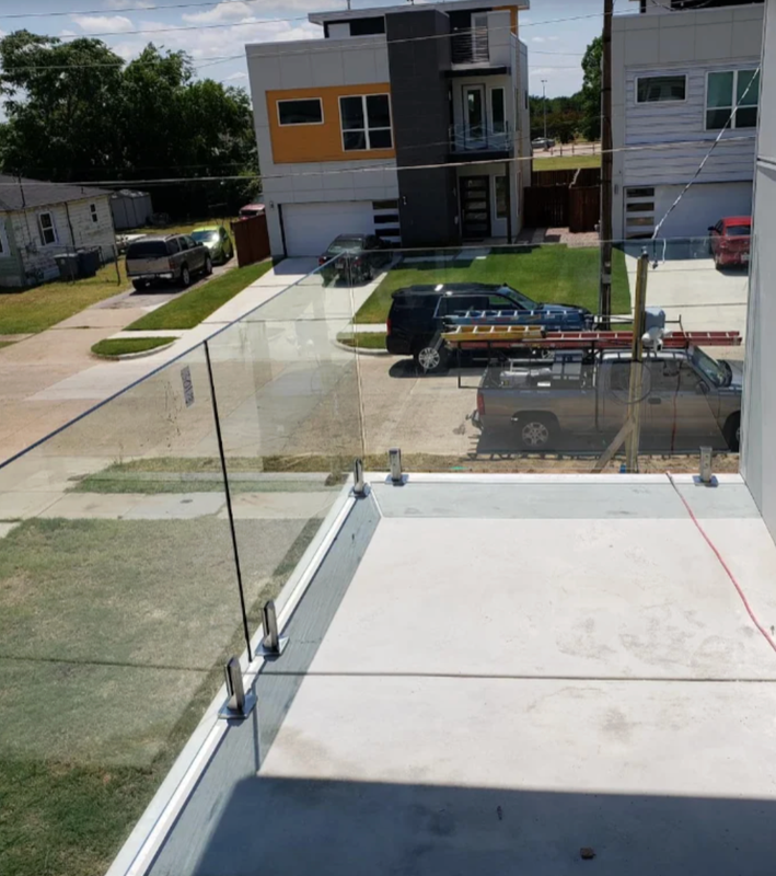 Balcony with glass railing overlooking a parking lot and modern apartment buildings under a sunny sky