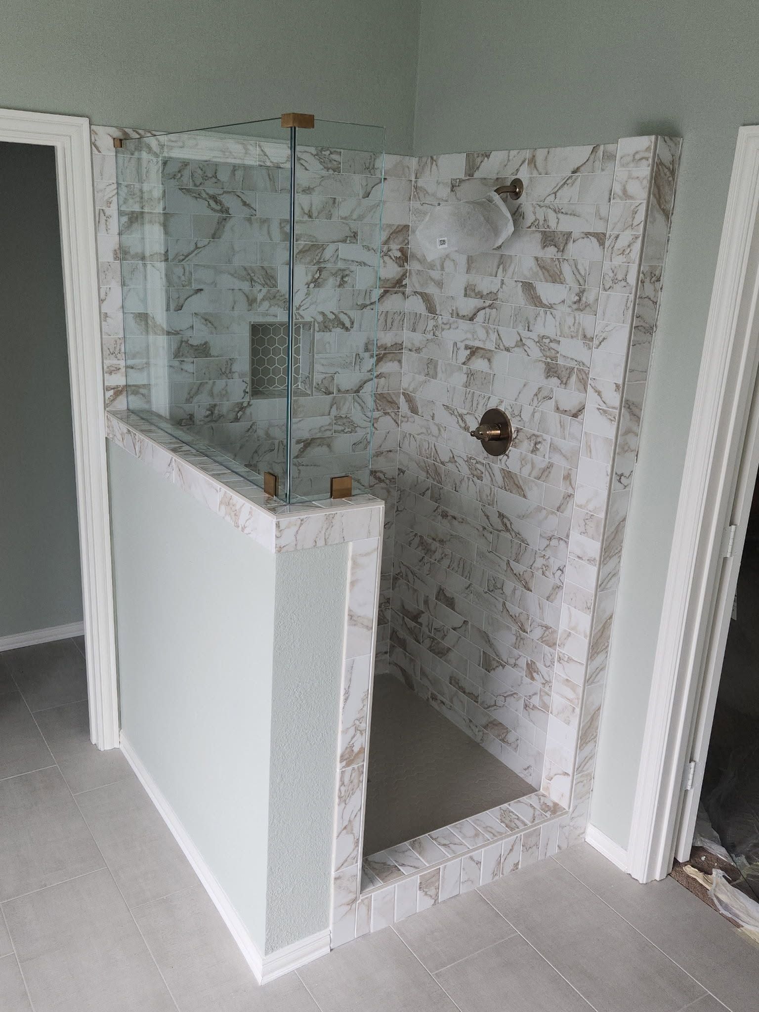 Tiled shower stall with a half-wall and glass panel in a bathroom under renovation