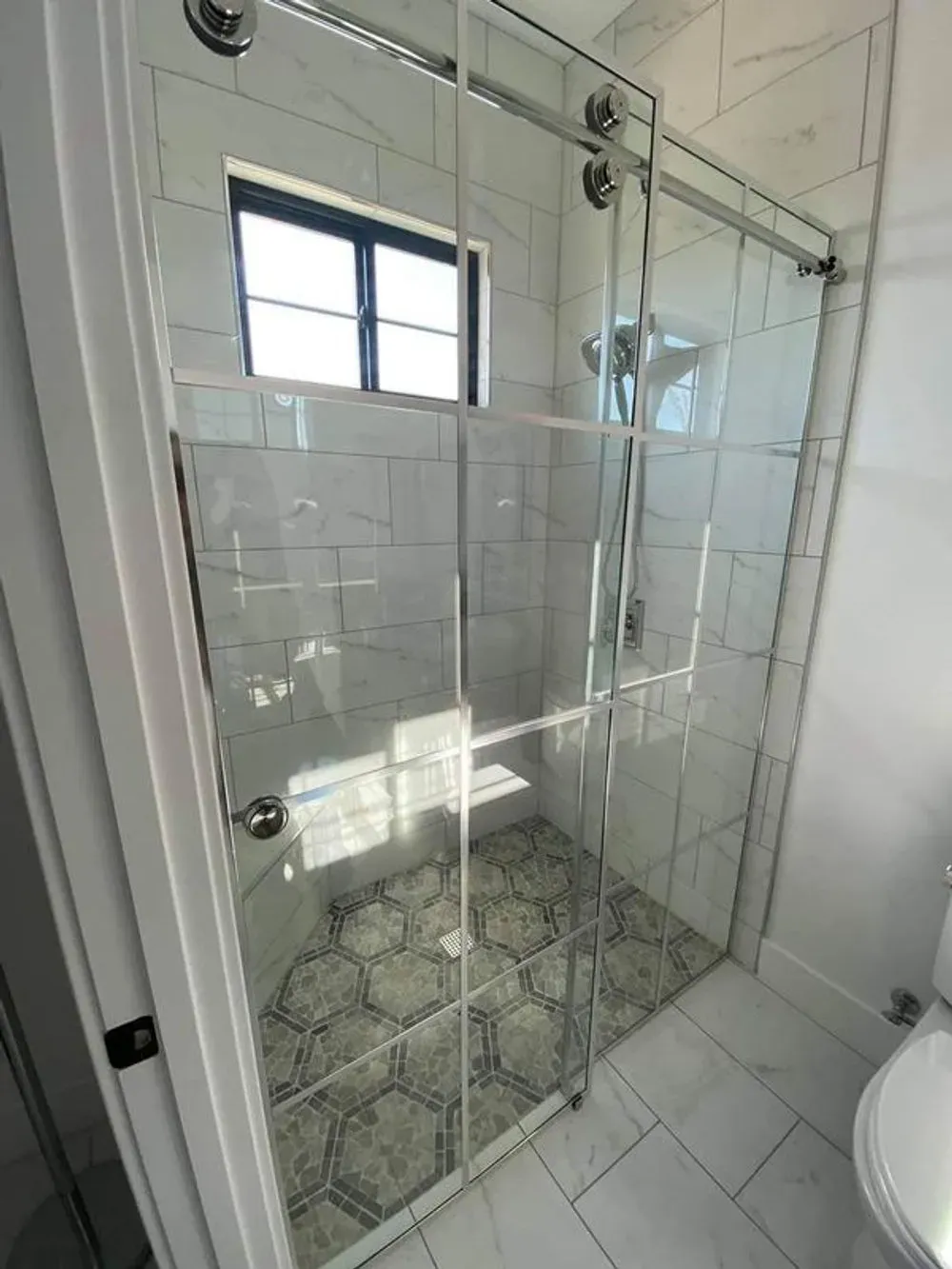 Glass shower enclosure with white tiled walls and patterned floor in a bathroom