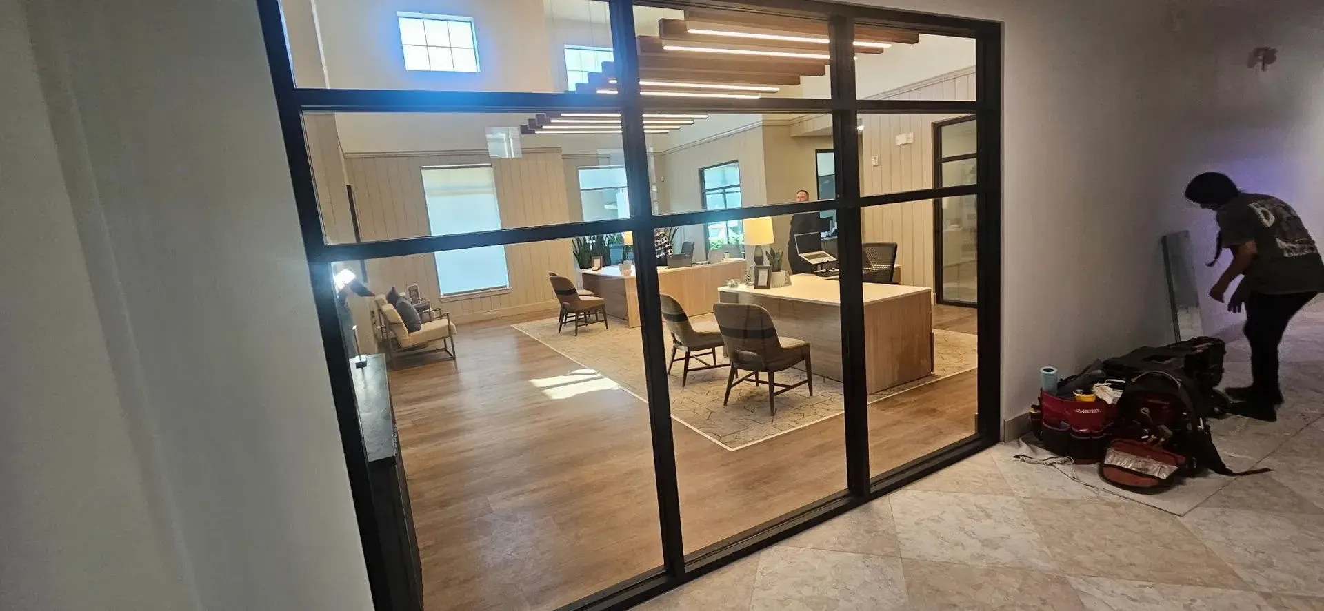 Glass-walled office lobby with chairs inside and a person standing near bags by the entrance