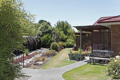 A brick house with a walkway leading to it and a bench in front of it.