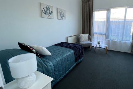 A bedroom with a bed , chair , table and lamp.