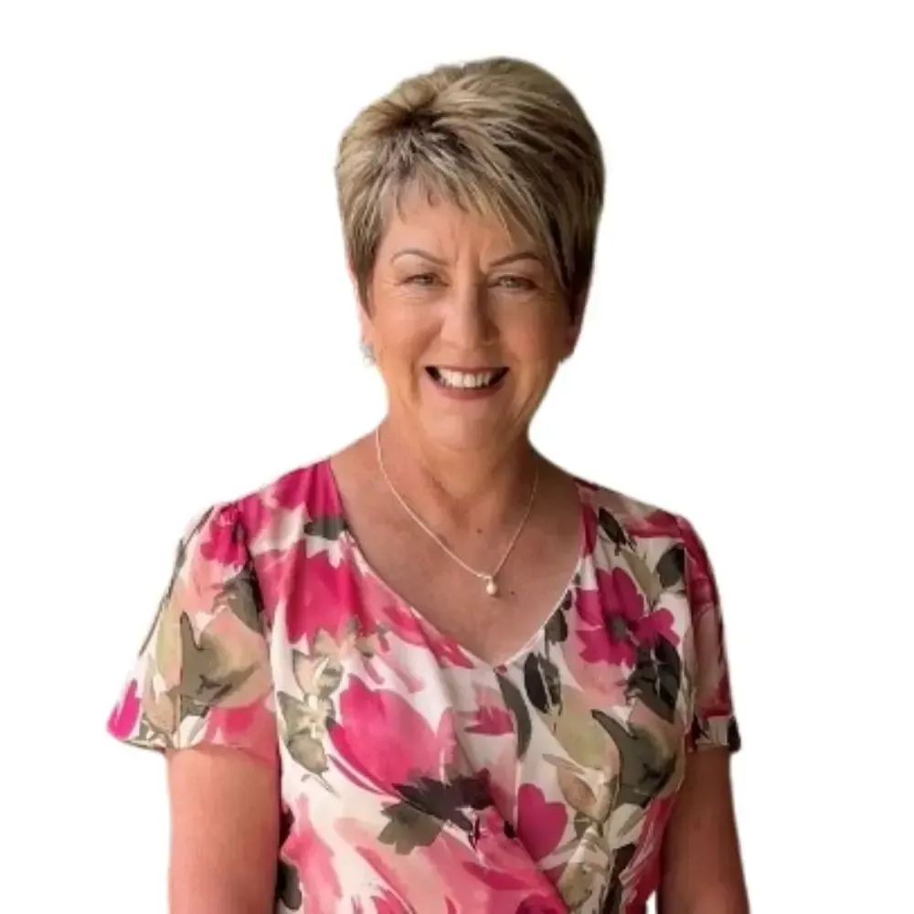 A woman in a floral dress is smiling in front of a white wall.