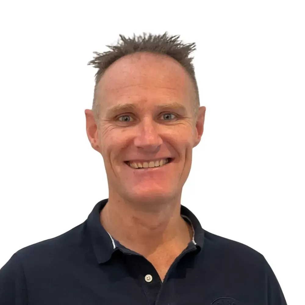 A man in a blue polo shirt is smiling in front of a white wall.
