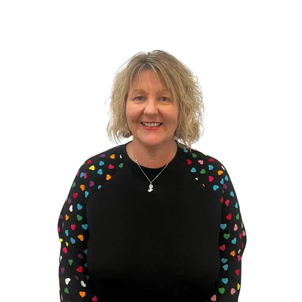 A woman wearing a black sweater with hearts on the sleeves is standing in front of a white wall.