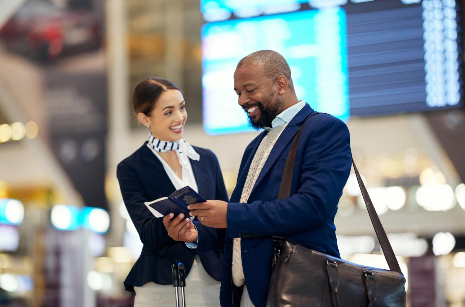 Two travelers smiling at an airport, looking at a map and suitcase near a flight information board