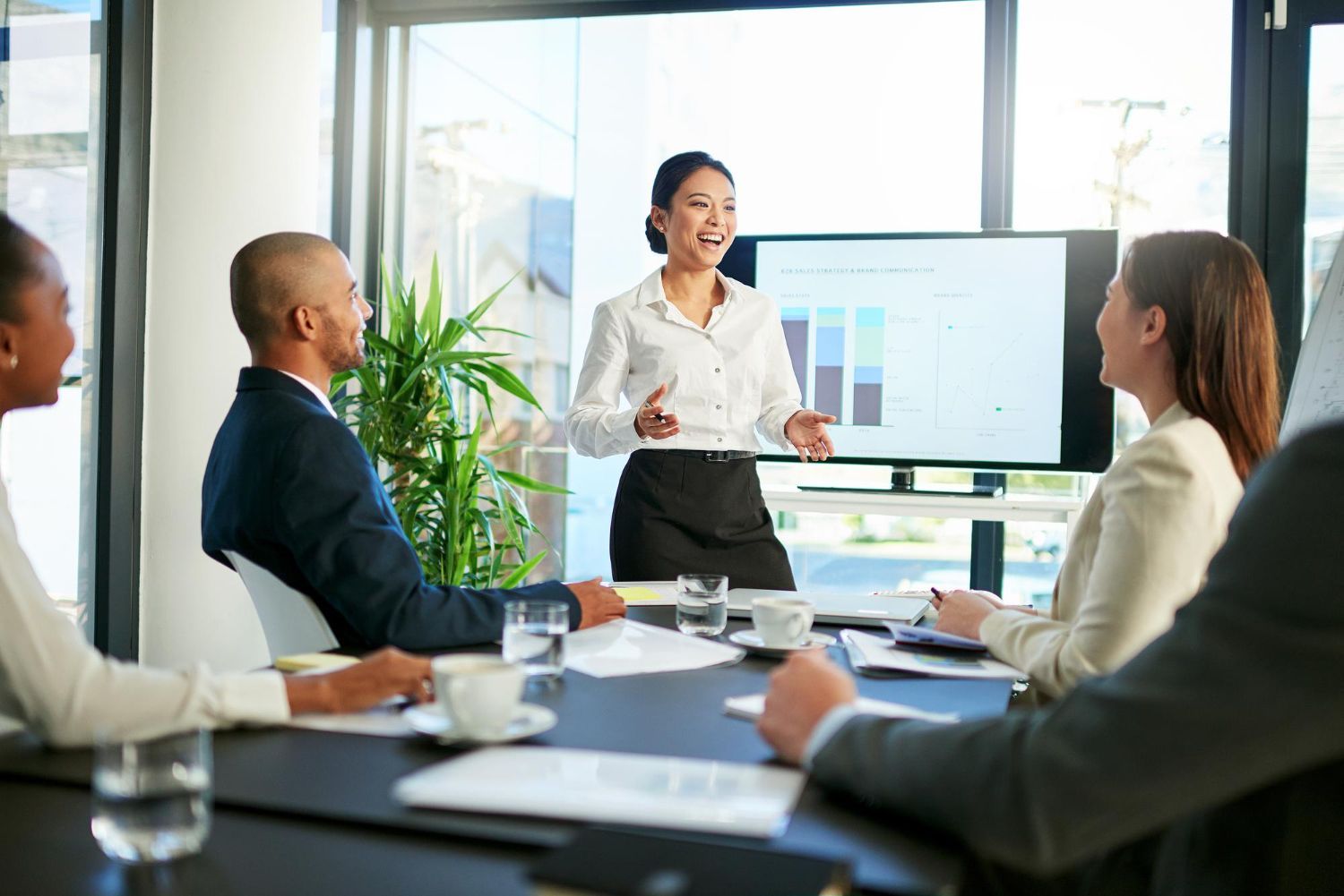 Business team in a meeting, with a presenter speaking beside a large presentation screen