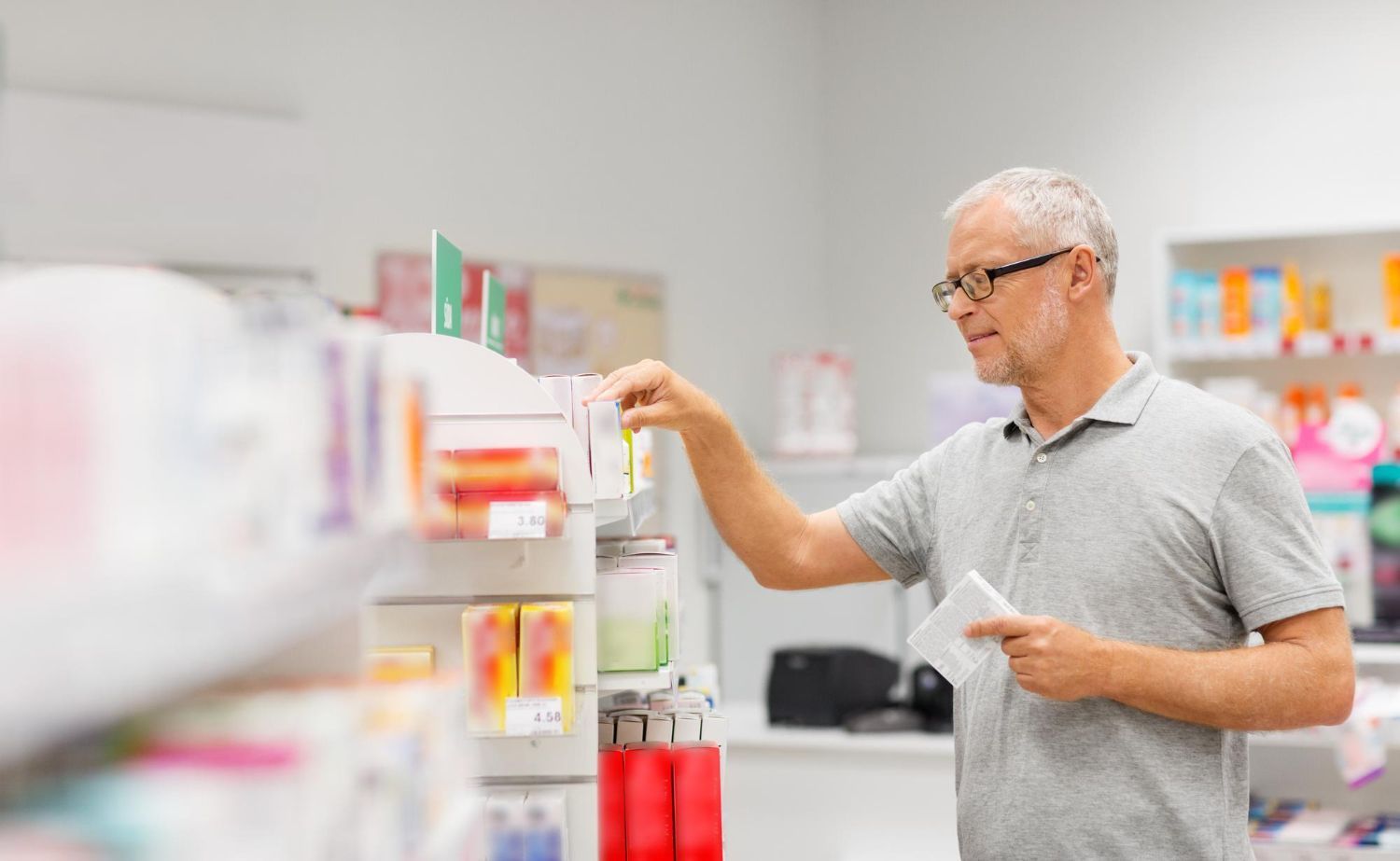 Man in a pharmacy aisle reaching for a product on a shelf