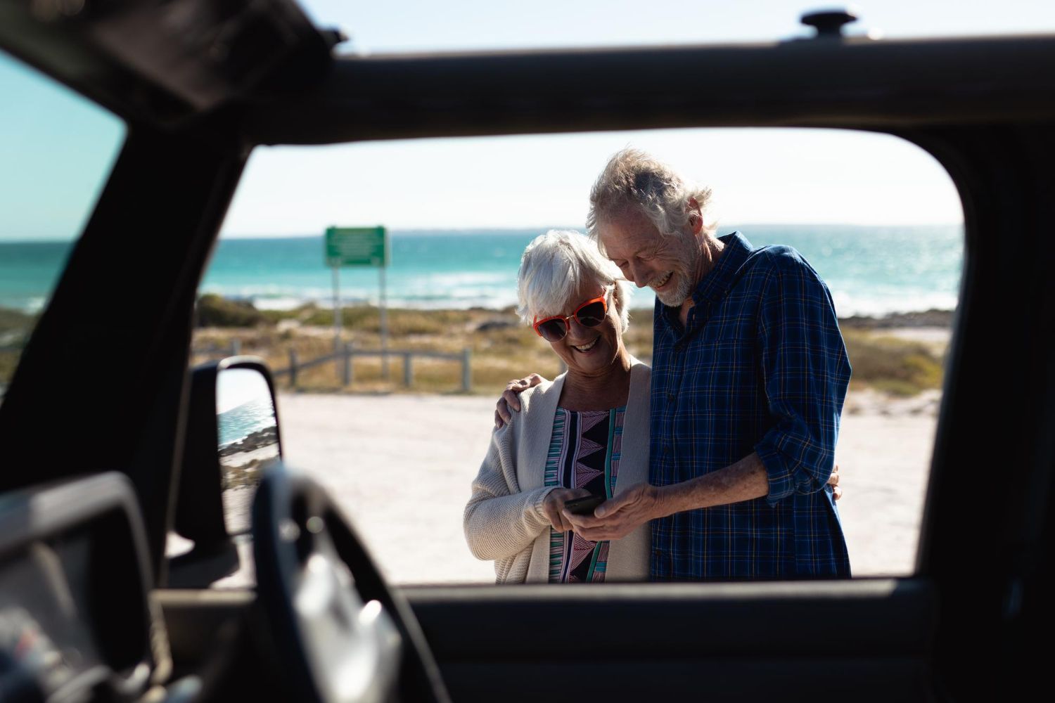 Two people stand beside a car, looking at a map in a sunny roadside parking area.