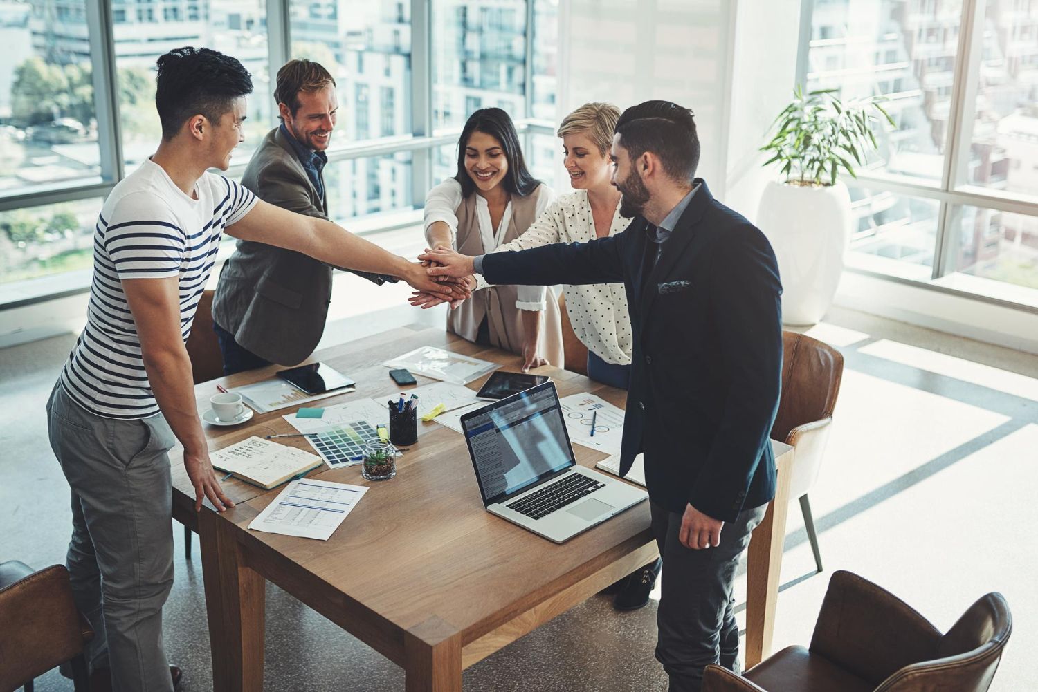 Team members shaking hands around a laptop in a bright office meeting room