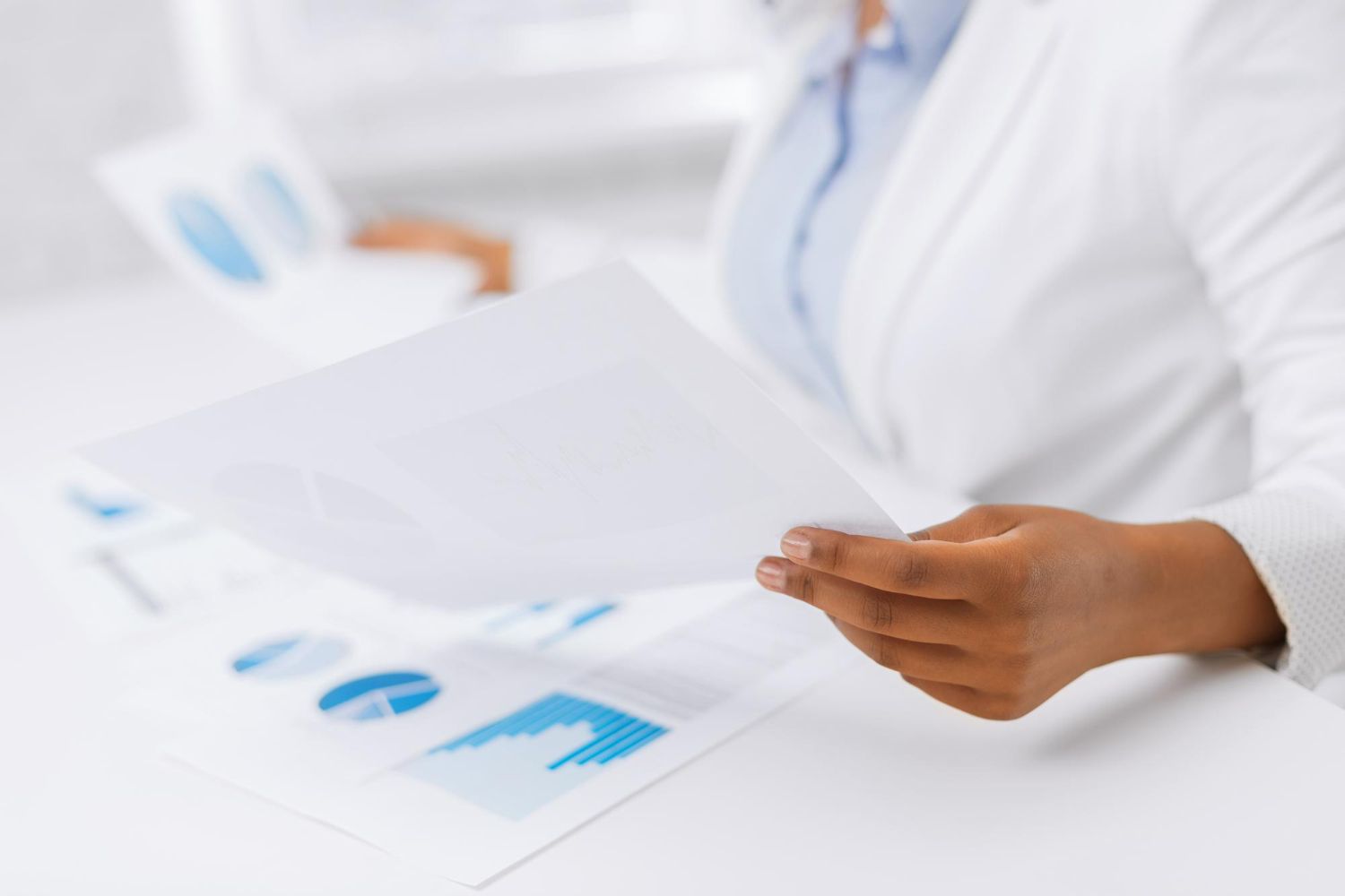 Person in white coat reviewing documents with blue charts on a desk