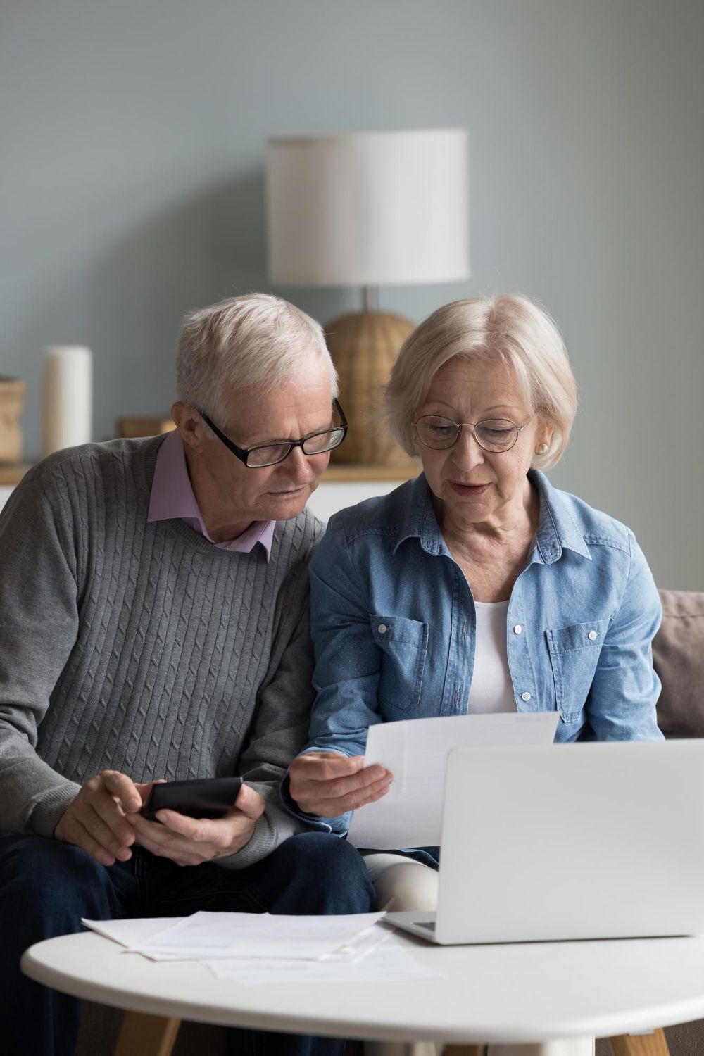 Two people reviewing documents at a table with a laptop in a living room