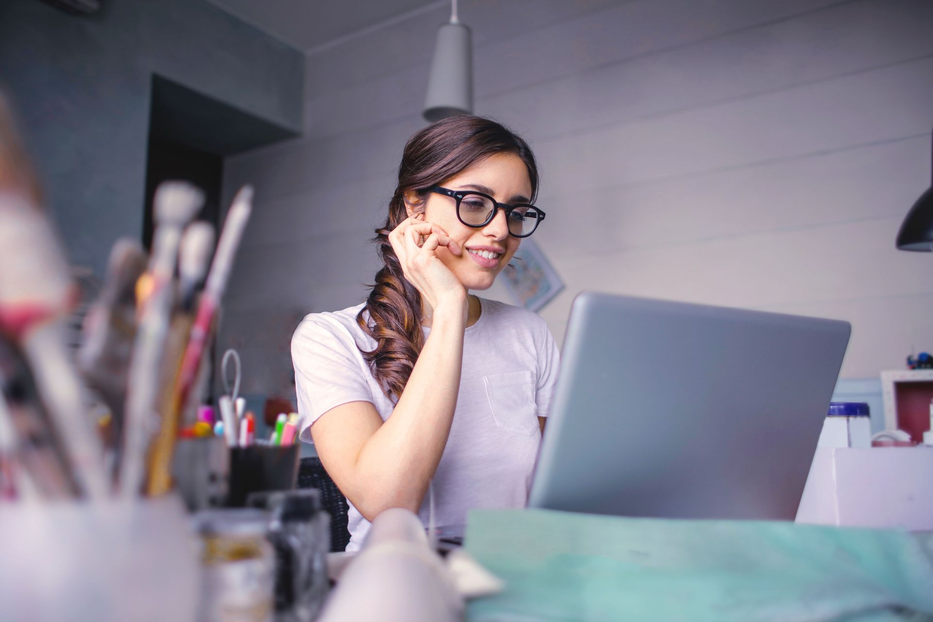 Person with glasses works on a laptop at a desk in a bright office or studio