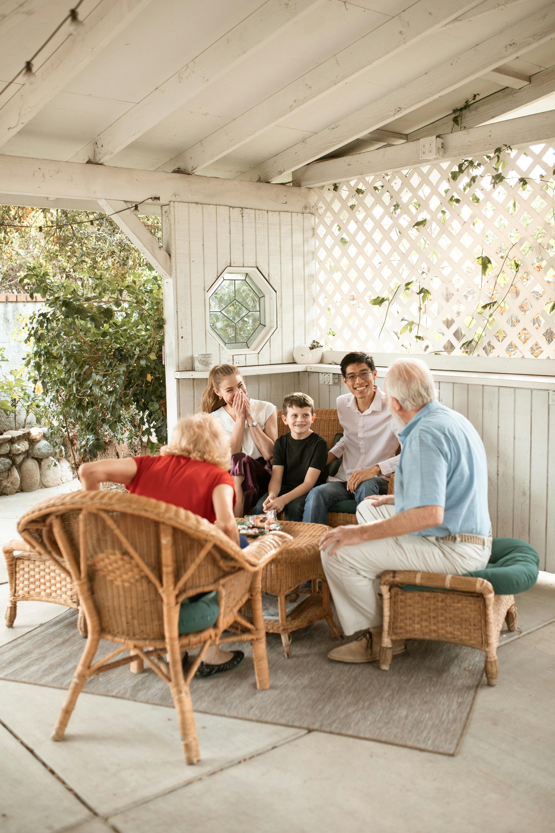 Group seated on wicker chairs in a bright porch, chatting around a small table.