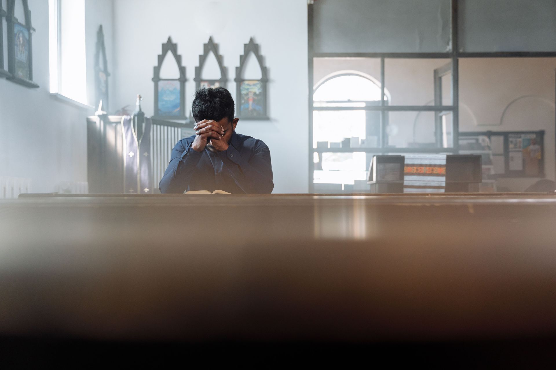 Person sitting alone in a bright room, resting their head on one hand behind a blurred foreground.