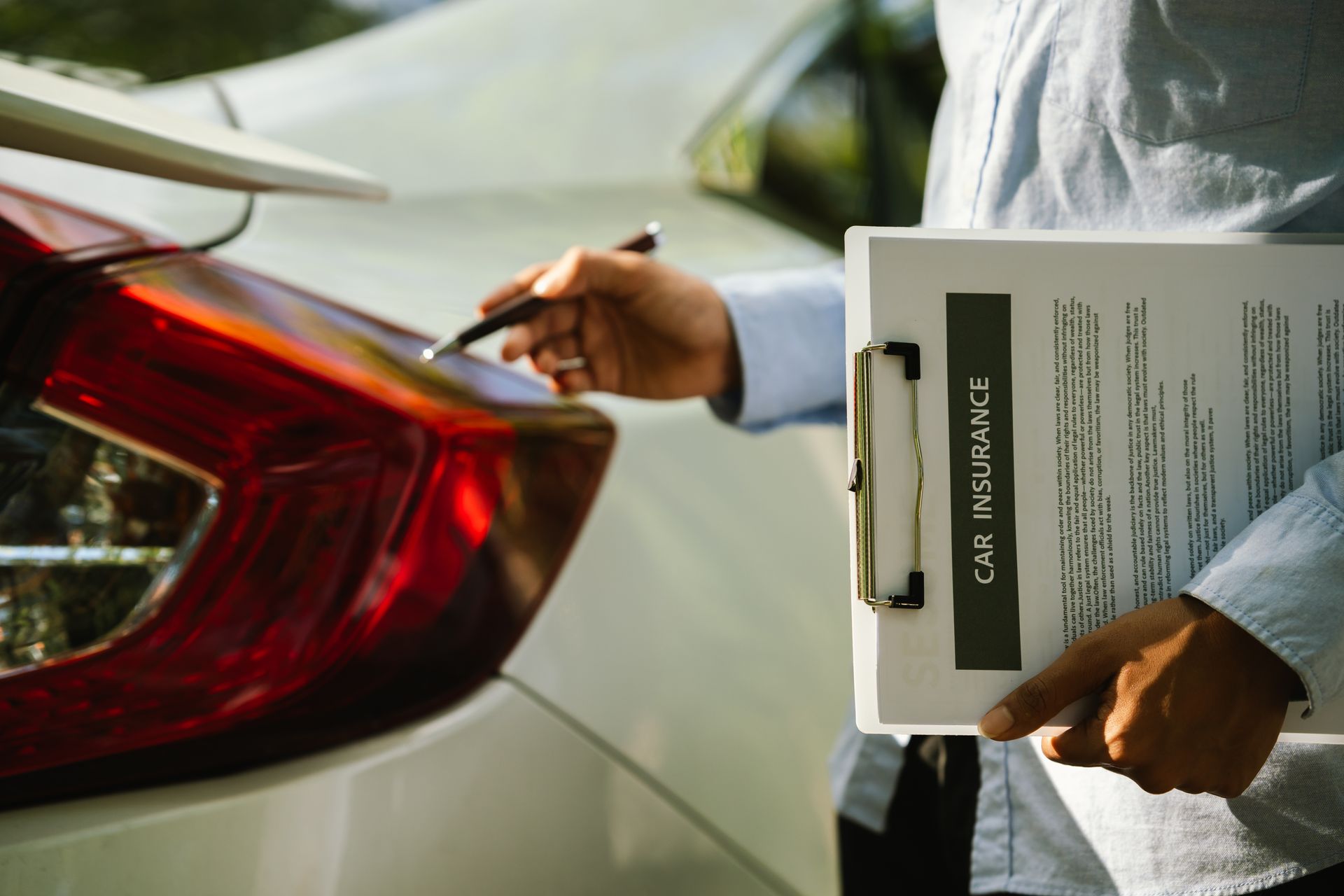 An insurance agent inspecting a car's taillight while holding a clipboard labeled Car Insurance