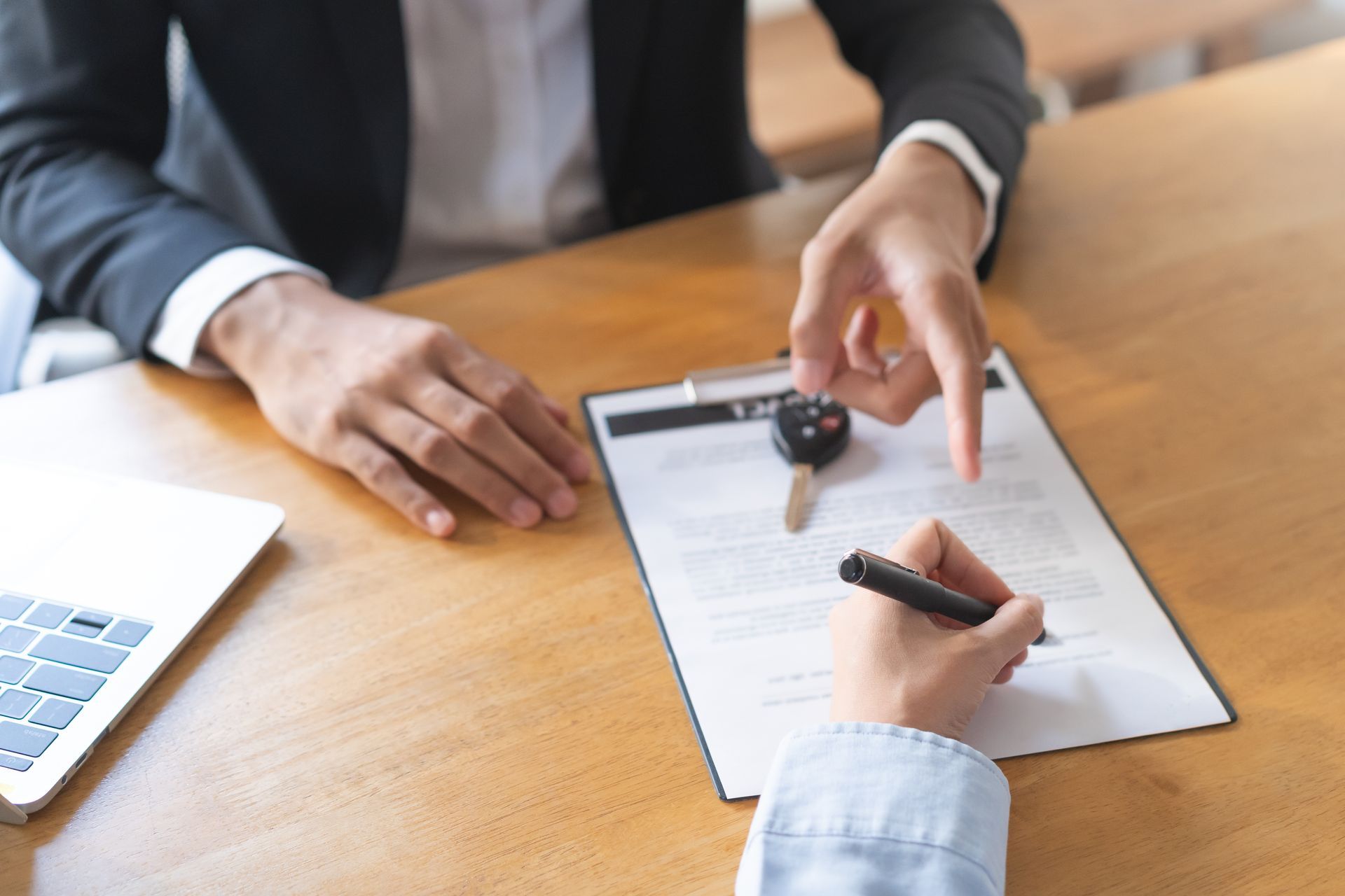 An agent pointing to a policy document while the client signs, car keys on clipboard