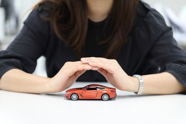 Hands gently cupping a small car model, symbolizing protection and insurance coverage Hands gently cupping a small car model, symbolizing protection and insurance coverage