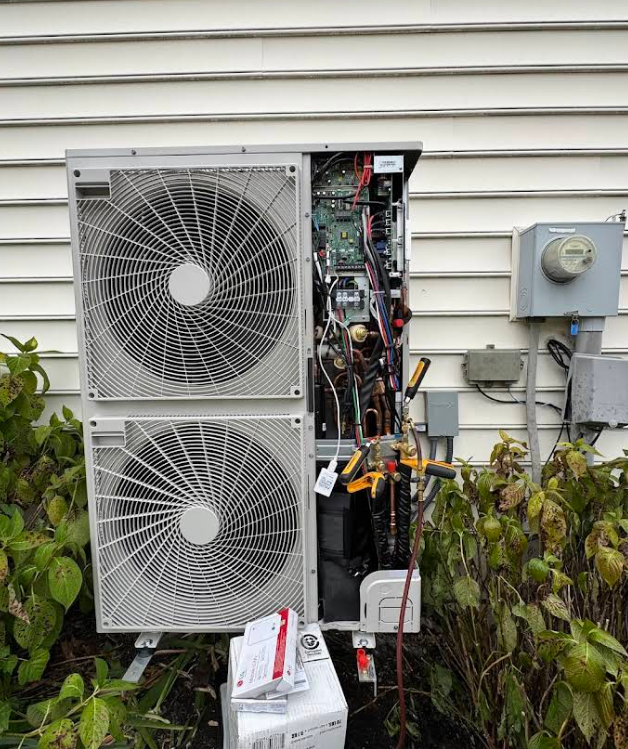 Outdoor air conditioning unit with open panel for repair; tools and wires visible.