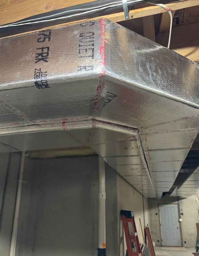 Insulated HVAC ductwork, silver, turning a corner in a basement.