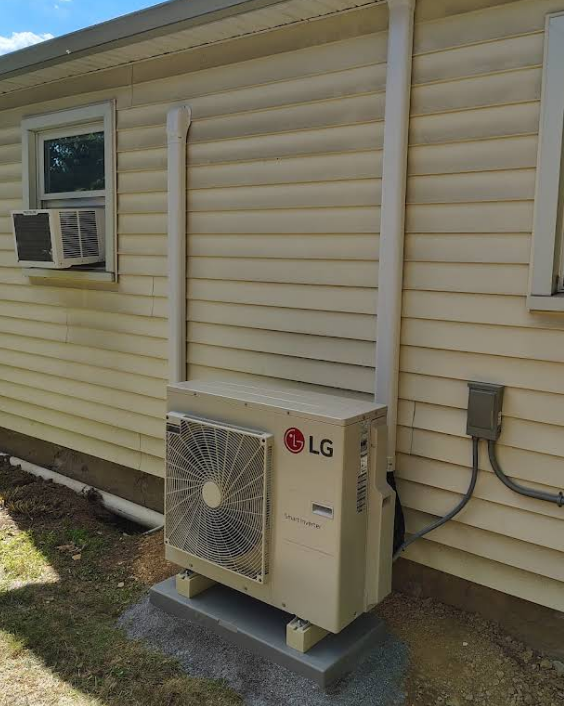 LG heat pump unit mounted on concrete, with connected white pipes on a building's exterior.