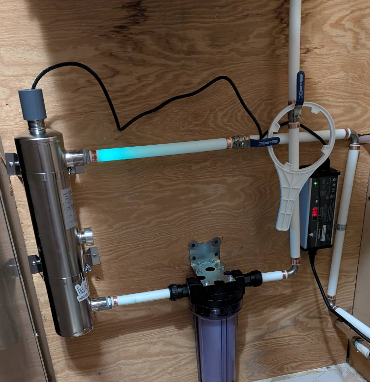Water filtration system with glowing ultraviolet light and filter. Piping on wood panel.