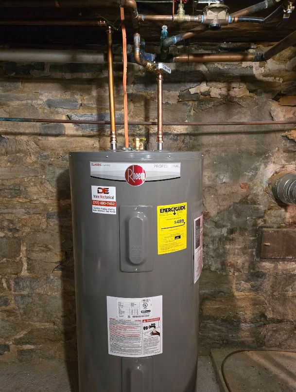 A Rheem water heater in a basement with copper pipes overhead against a stone wall.