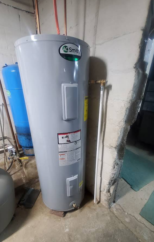 A tall, gray A.O. Smith water heater in a basement. Copper and white pipes are attached. 