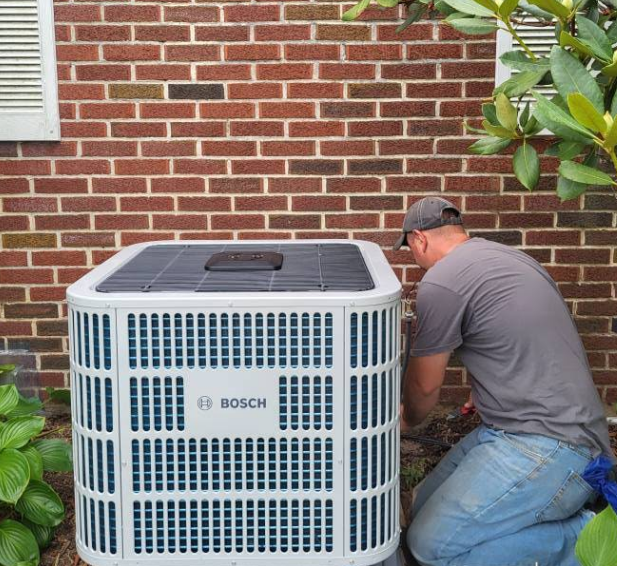 A man working on a Bosch air conditioning unit next to a brick wall and bushes.