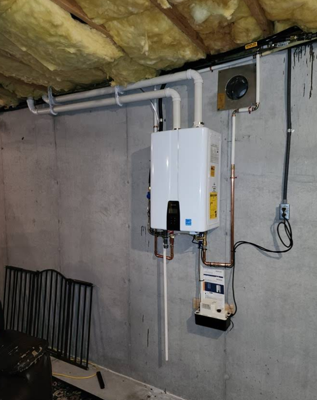 Tankless water heater installed on a concrete wall with piping, vent, and gas meter in a basement setting.