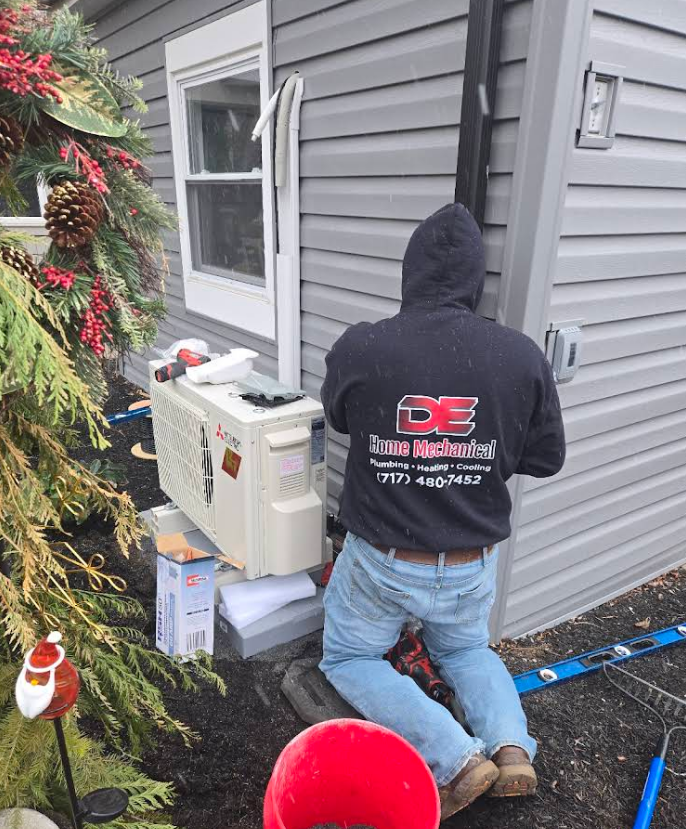 Person in hoodie installing an outdoor HVAC unit on a building.
