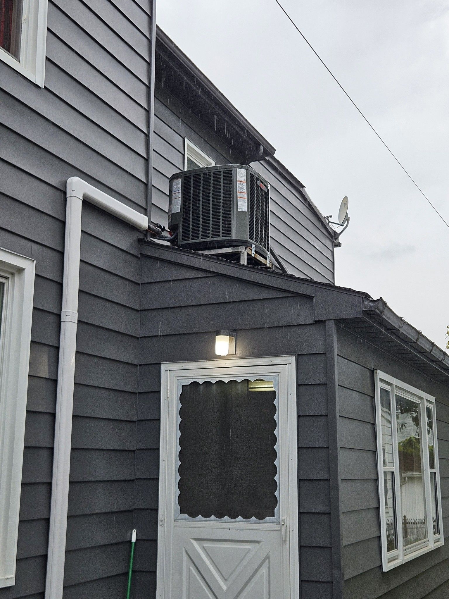 Gray house exterior with an air conditioning unit on the roof of a small porch with a screen door.