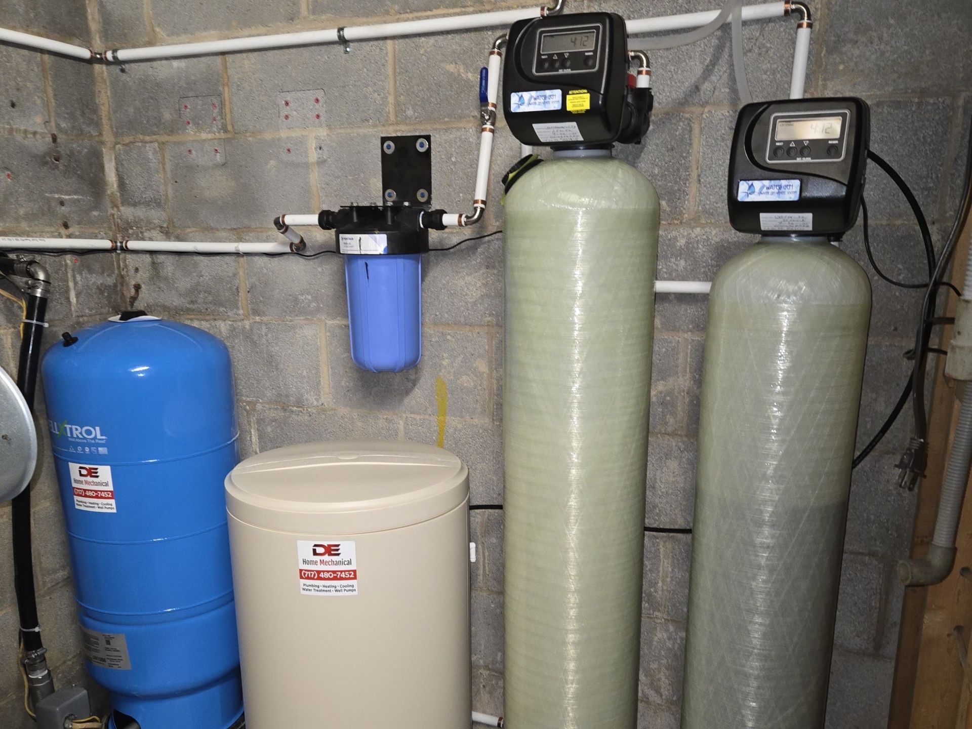Water filtration system with tanks, gauges, and pipes against a cinder block wall.