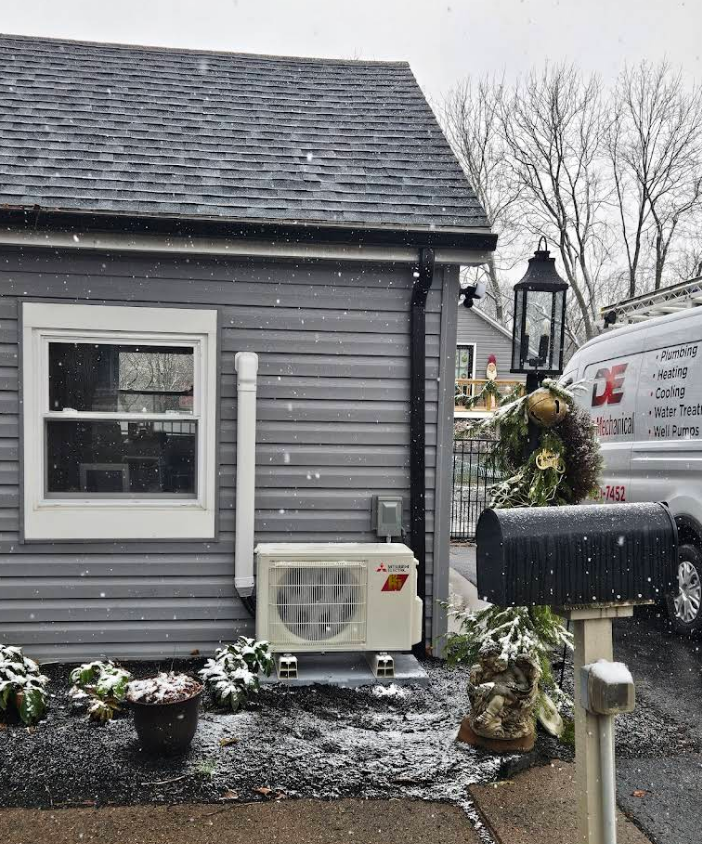 Exterior of a gray house with a window, AC unit, and mailbox in snowy conditions. A service van is parked nearby.
