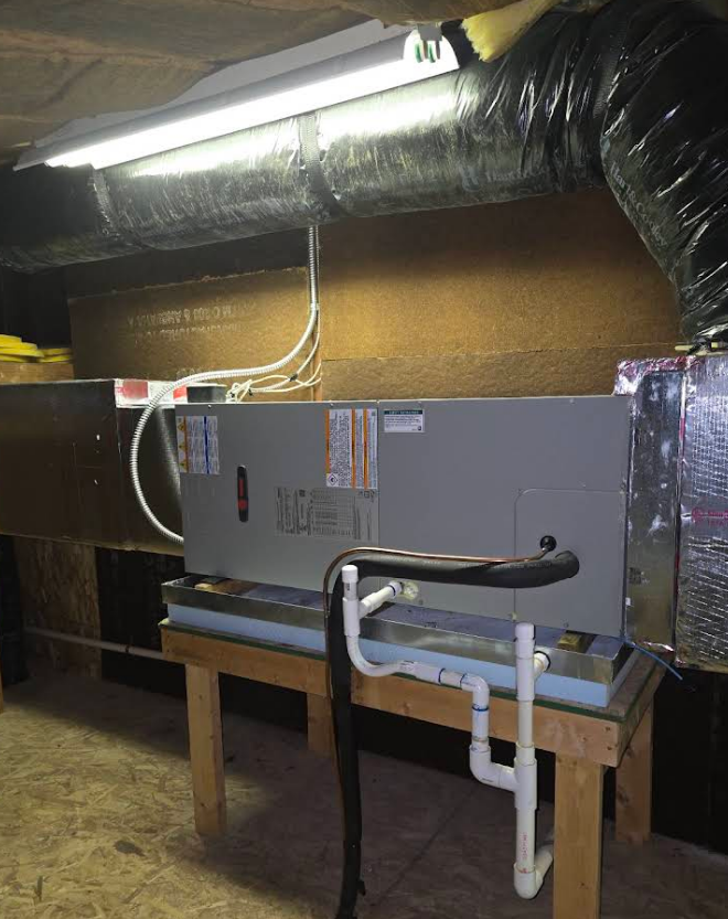 HVAC unit on wooden stand in a crawlspace, with ductwork and fluorescent lighting overhead.