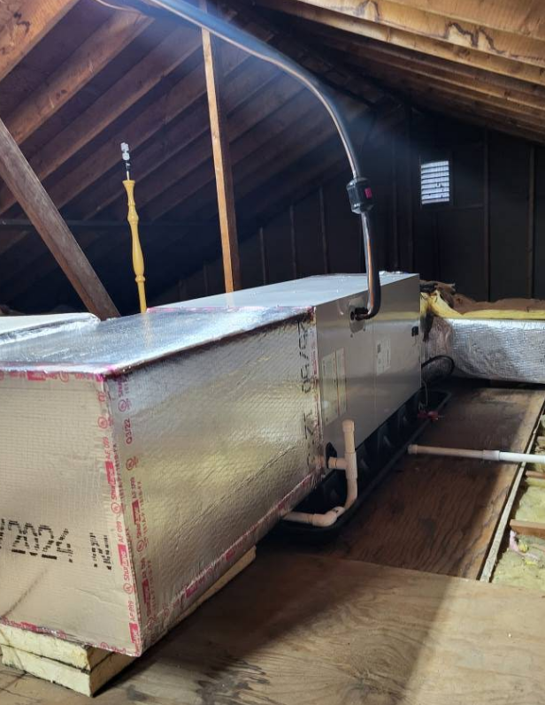 HVAC ductwork in an attic. Silver rectangular ductwork and connected black tubing in a wood-framed space.