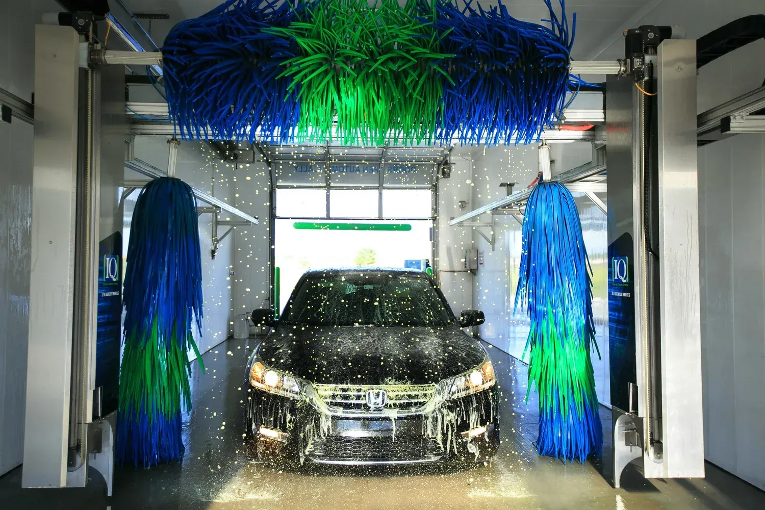 Car being washed in an automated car wash with blue and green brushes and water spray