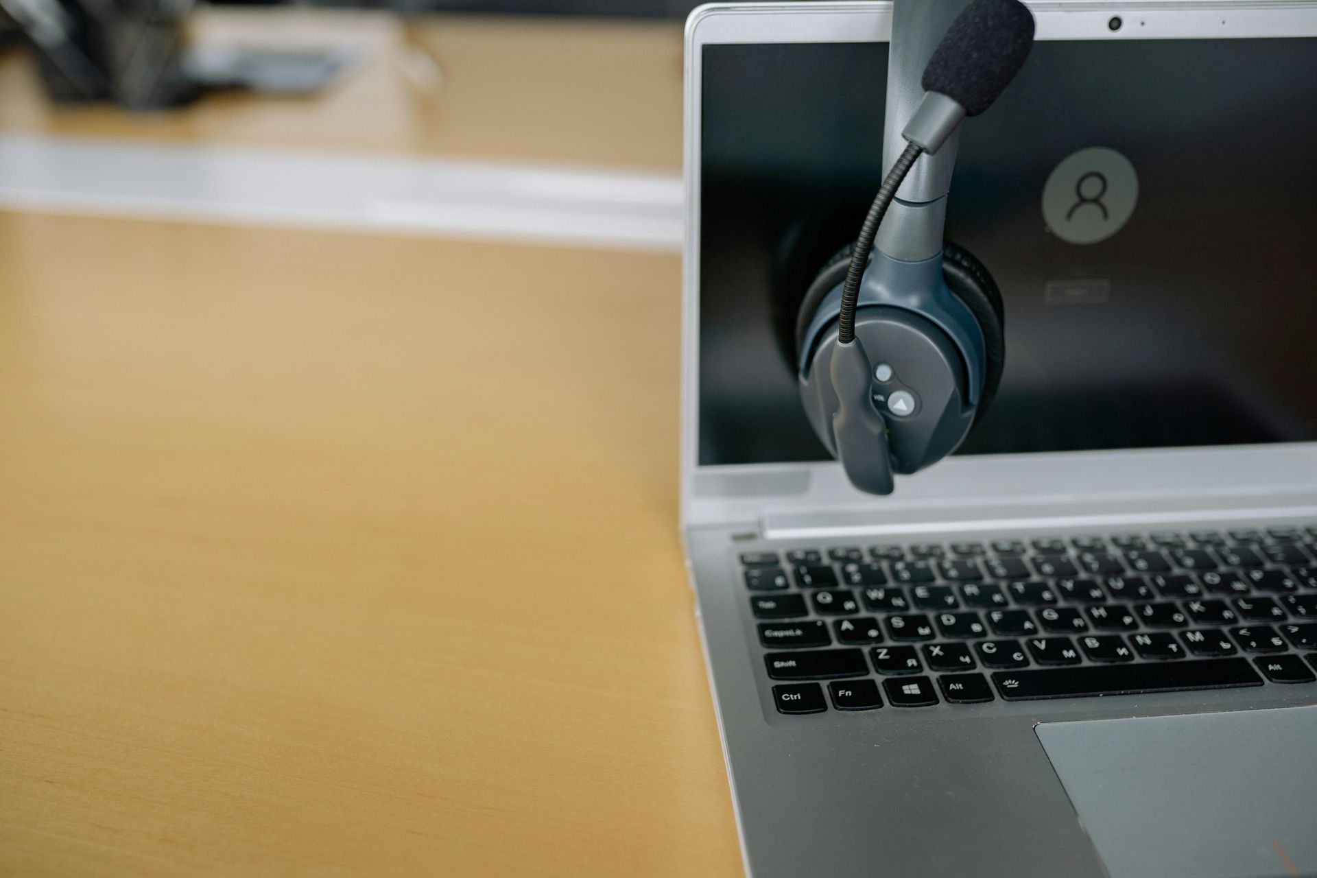 Laptop with headset hanging over the keyboard on a desk, with a blank screen in the background