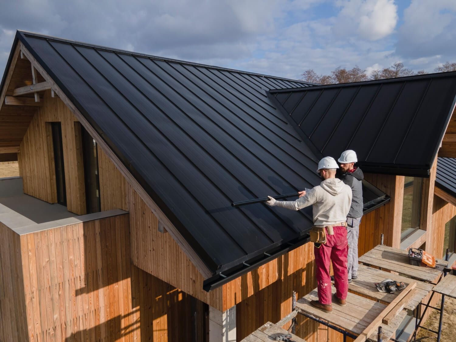 Two Brookland Roofing team members are installing a metal roof in cloudy weather conditions.