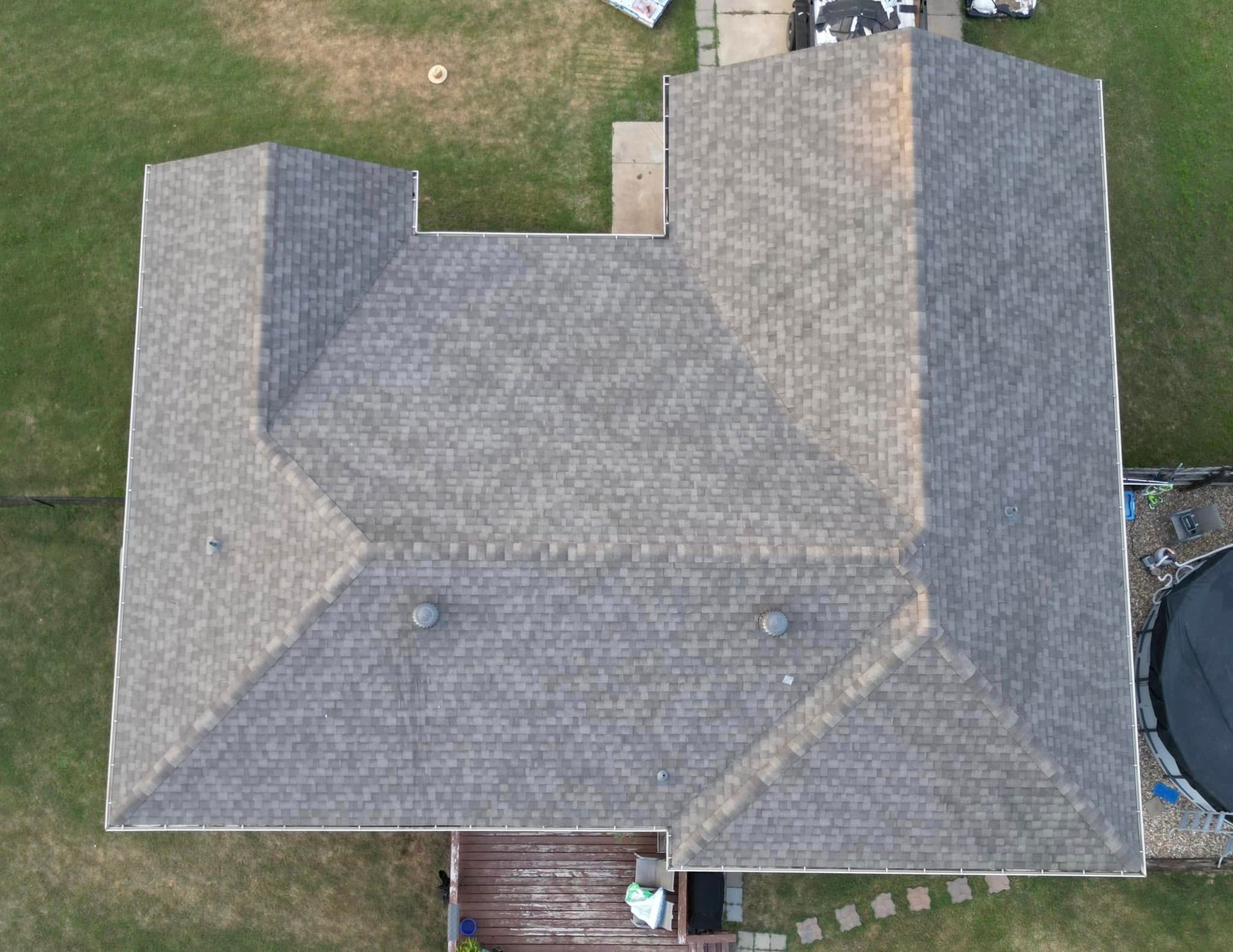 Overhead view of a house with a gray shingled roof, lawn surrounding the house and a small deck attached.