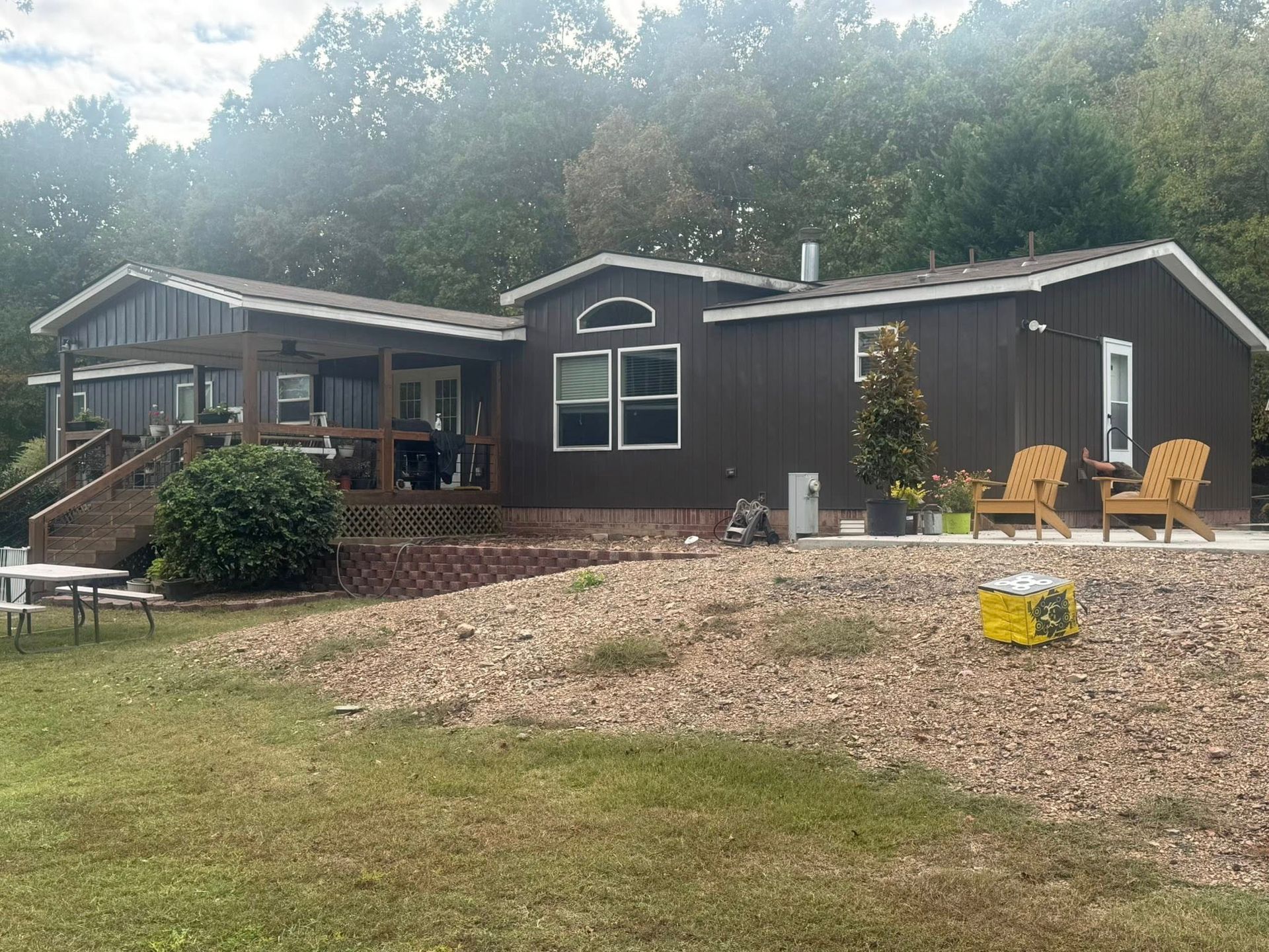 Brown house with porch, two yellow chairs, and picnic table on grassy hill.