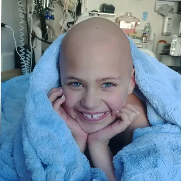 A bald child is wrapped in a blue blanket and smiling