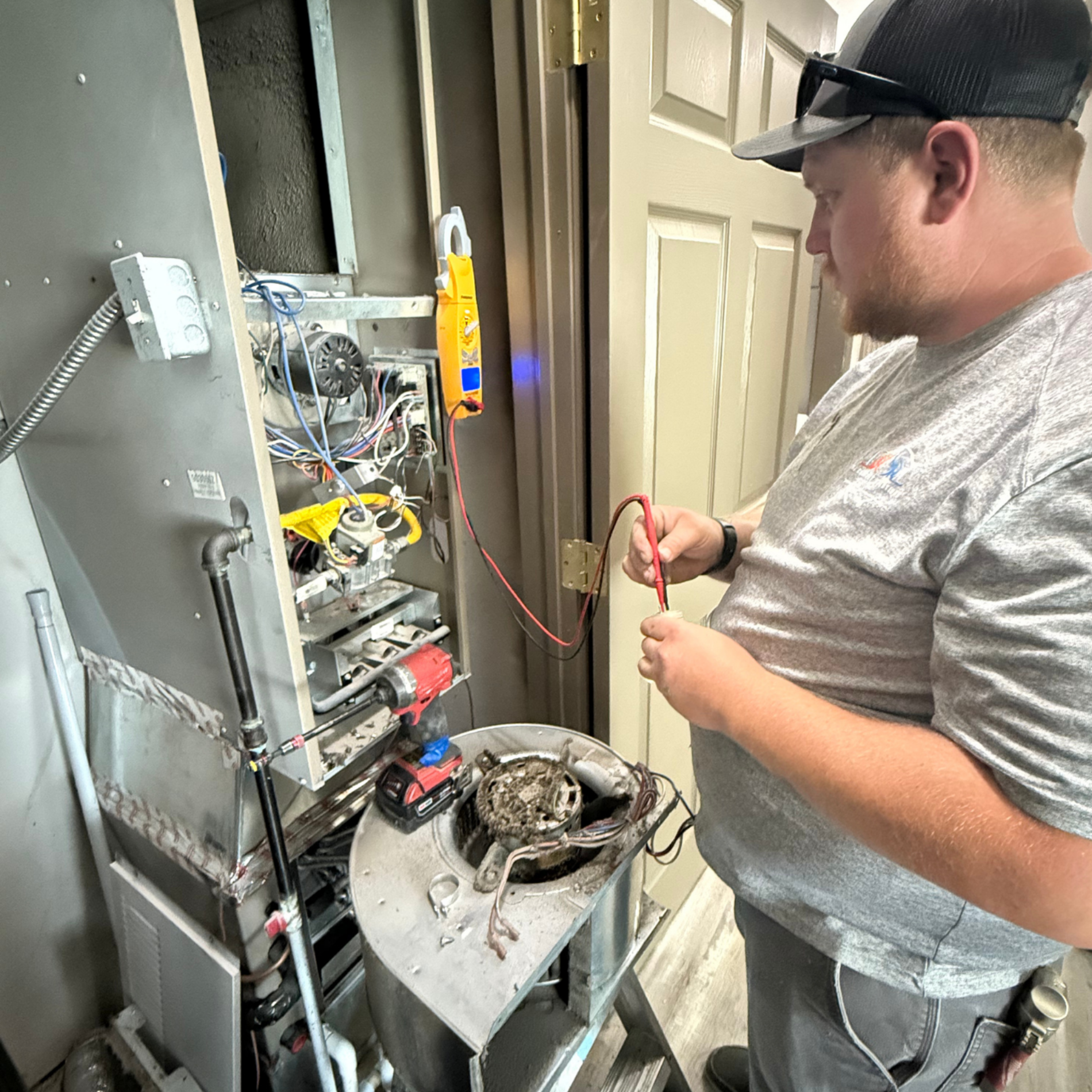 HVAC technician repairs furnace, using a multimeter in a utility room.