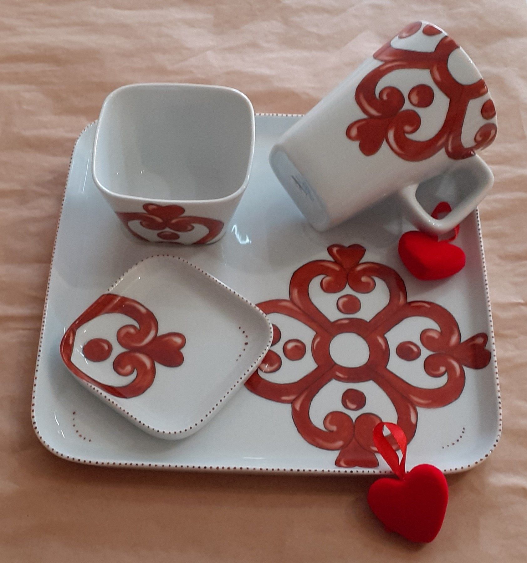 Set di piatti con motivi bianchi e rossi, composto da vassoio quadrato, ciotole e decorazioni a forma di cuore.