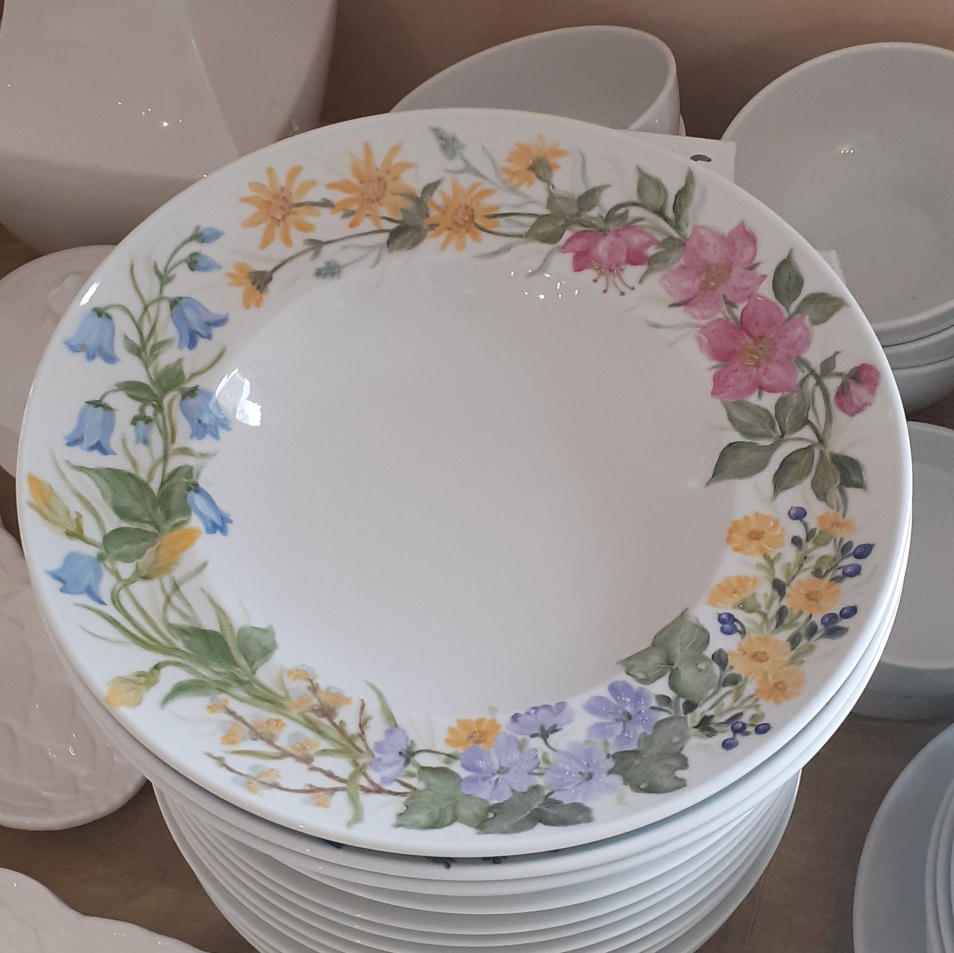 Piatto bianco con motivo floreale, impilato su altri piatti. I fiori sono gialli, rosa e blu.