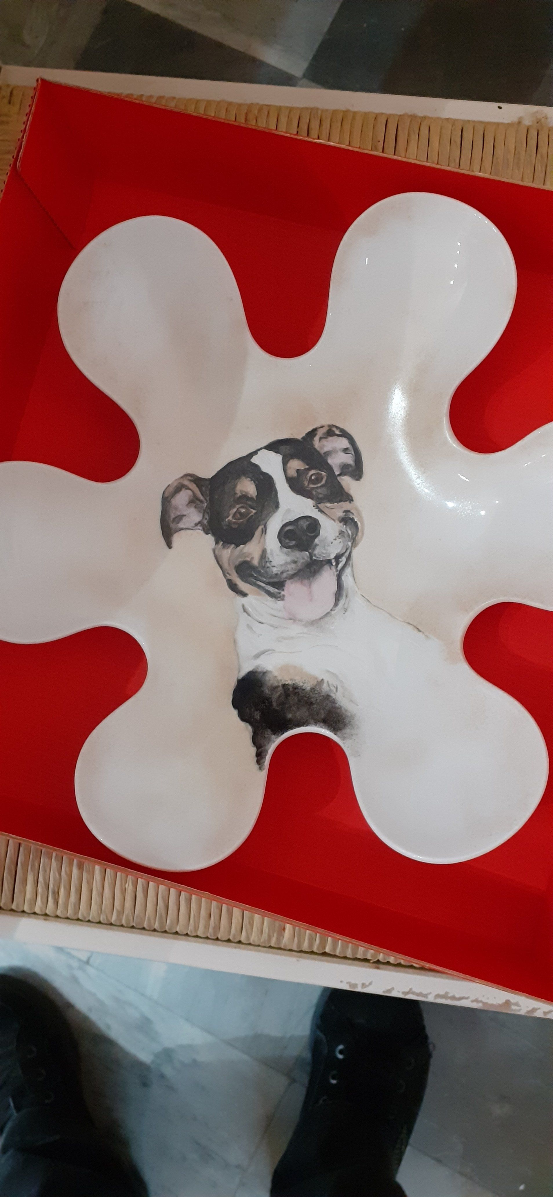 Ciotola bianca a forma di fiore su sfondo rosso, con all'interno l'illustrazione di un cane sorridente.